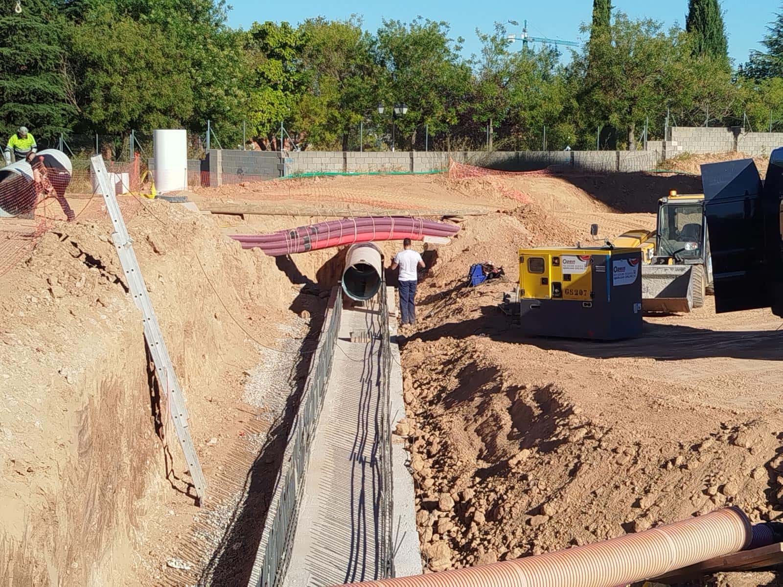 Zanja abierta con la conducción de acero apoyada sobre la solera de hormigón y un operario trabajando en la boca de la tubería.